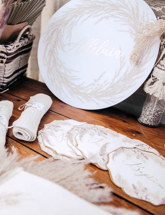 Mise en scène sur table des serviettes en papier pampas et fleurs de coton pour baptême dorées
