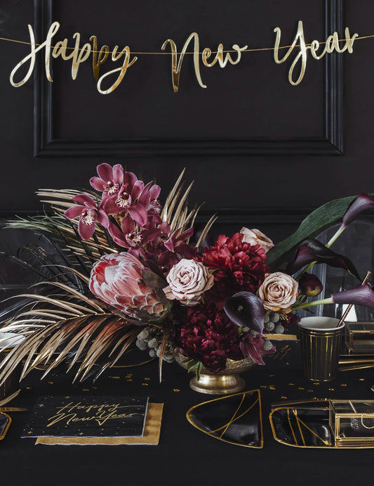 Mise en situation sur une table de fête des serviettes en papier Happy New Year noires et dorées avec décor étoilé