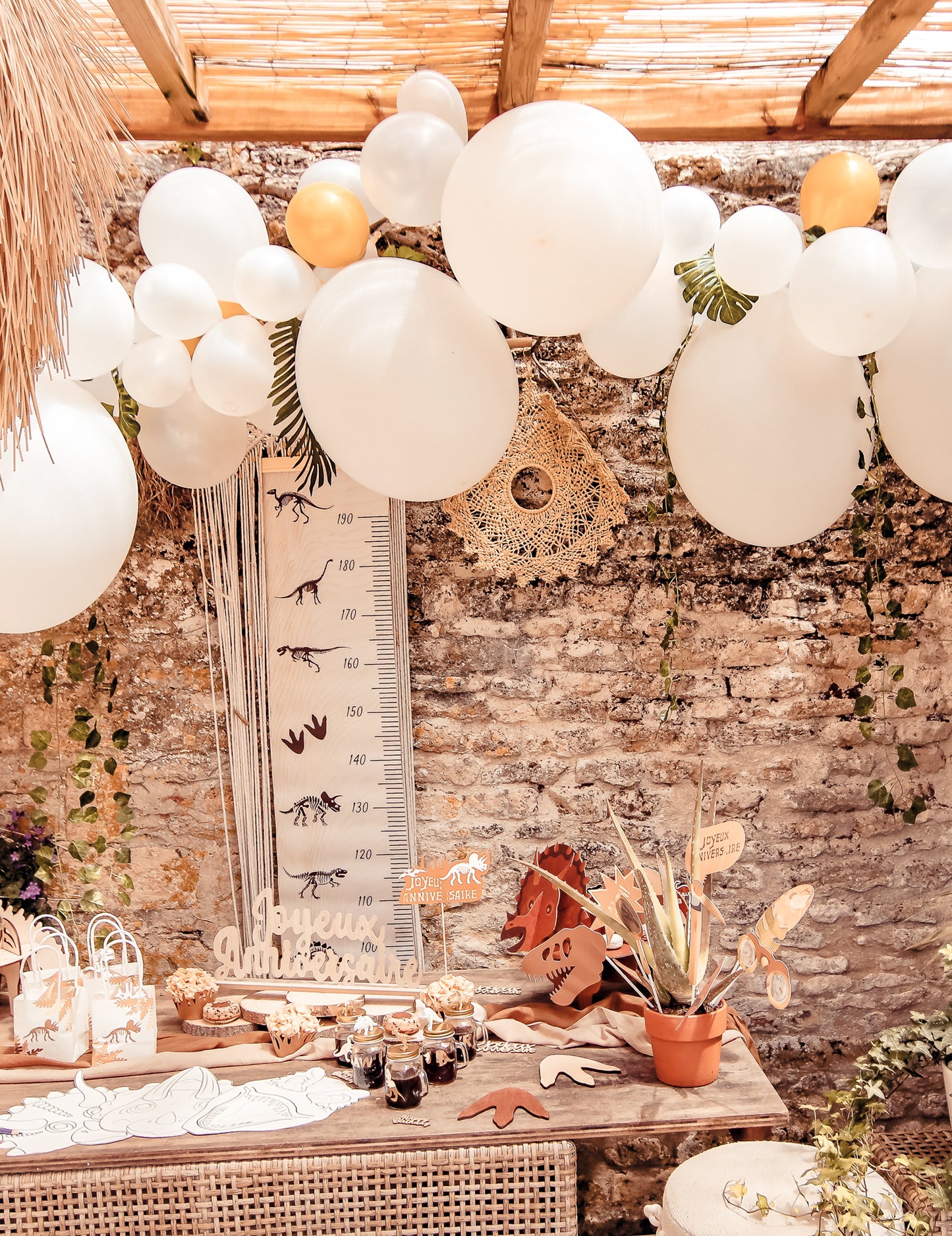 Mise en situation du kit arche de 55 ballons blanche et or avec lierre et feuilles tropicales