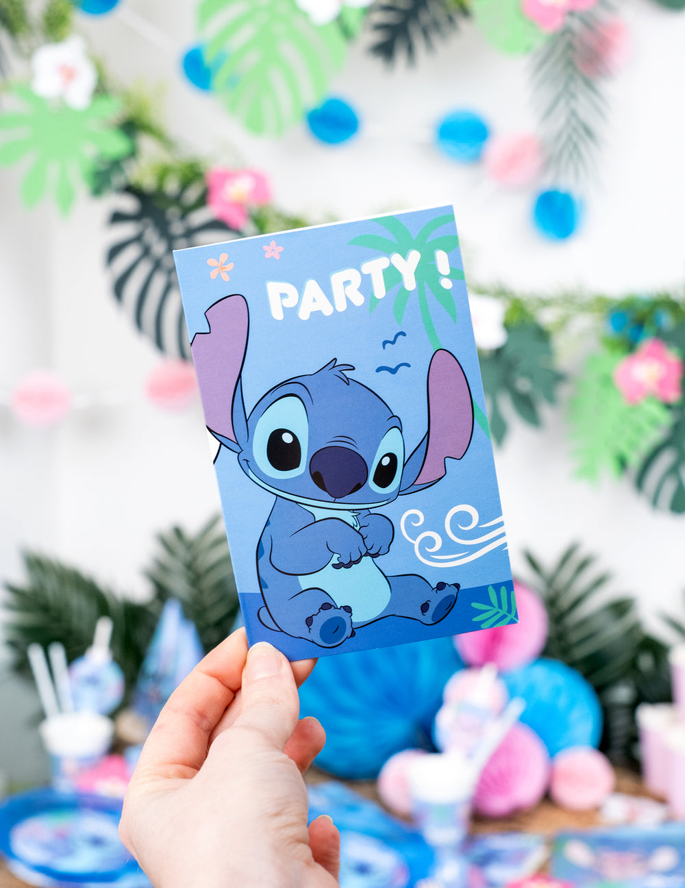 Gros plan sur la carte avec Stitch tenue en main des invitations et enveloppes Stitch
