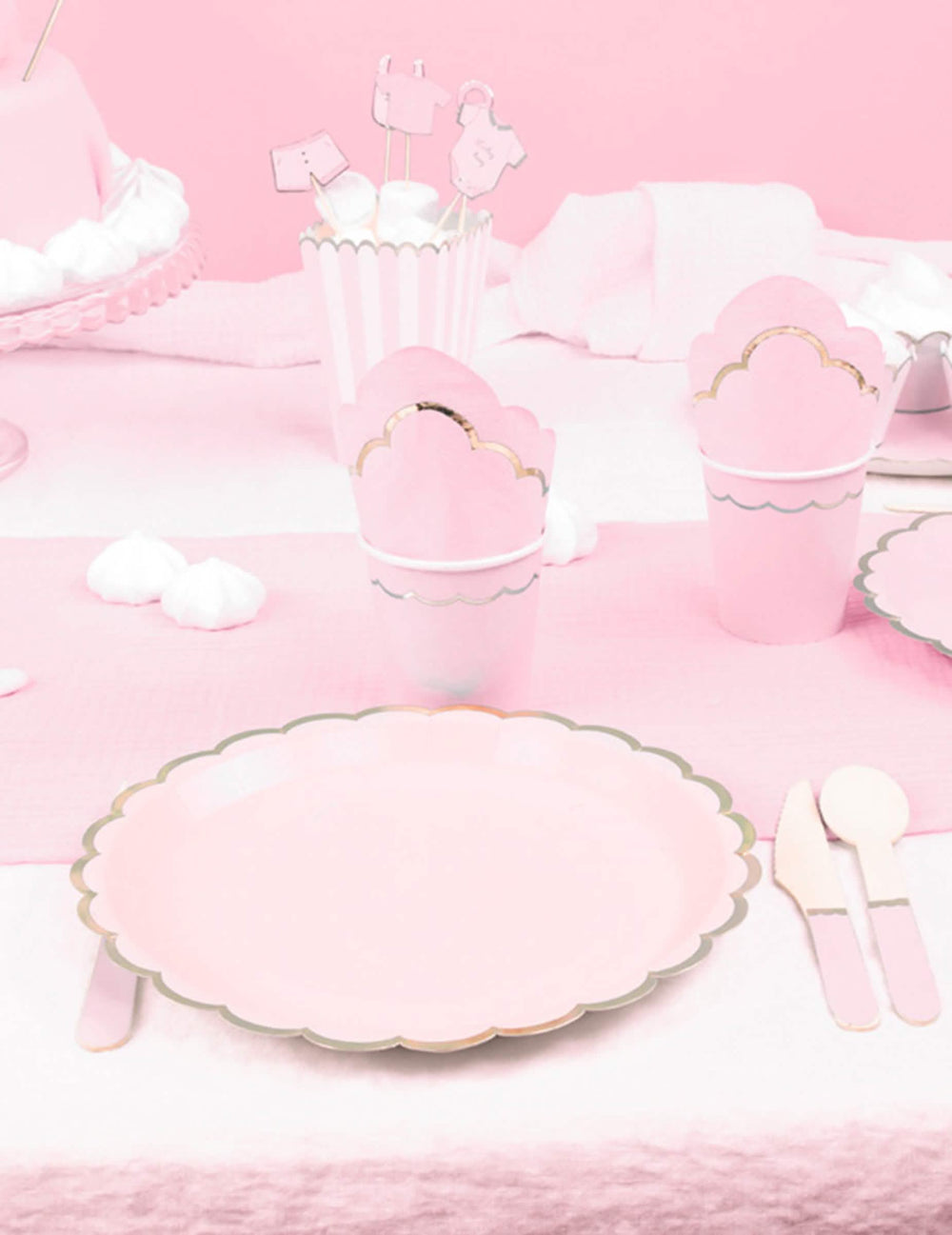 Mise en situation sur une table de fête des assiettes en carton festonnées rose pastel et or