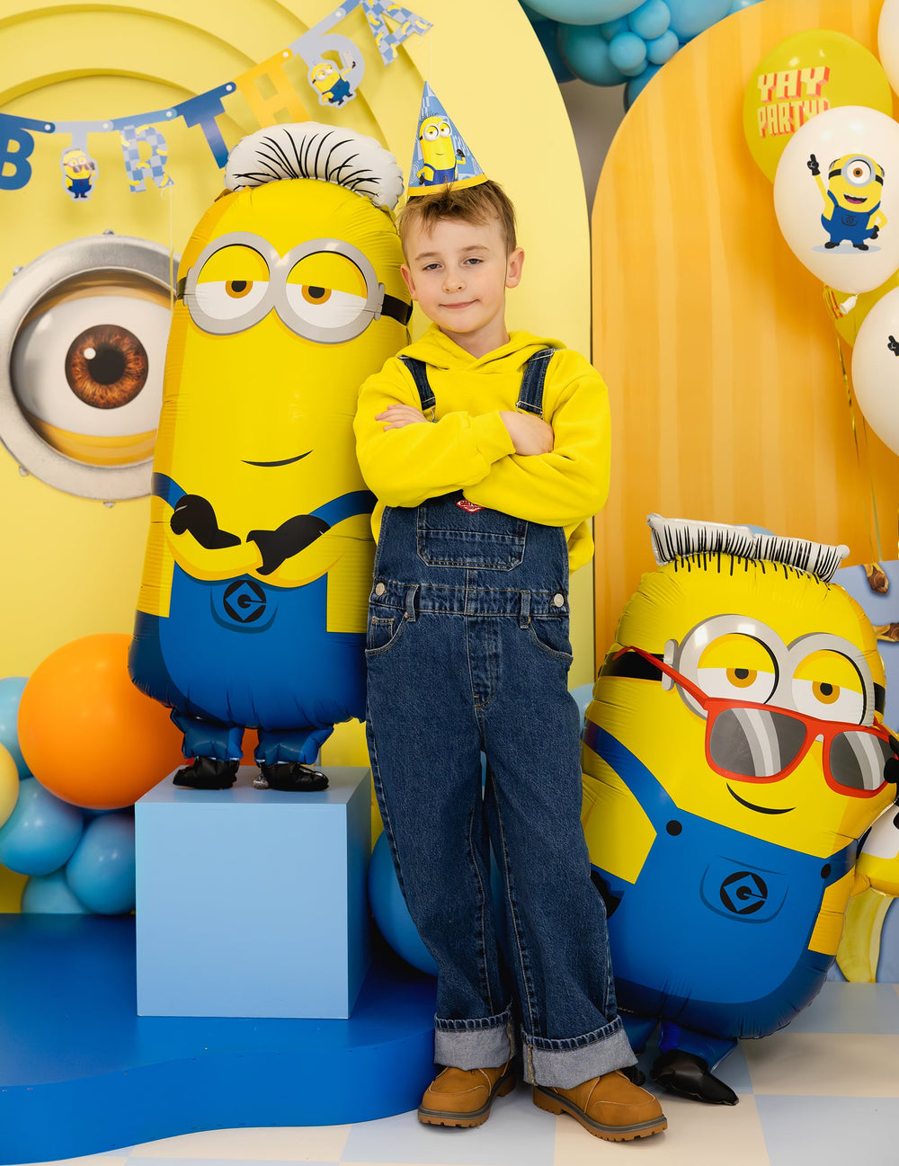 Enfant debout à côté du ballon aluminium Tim Minions™