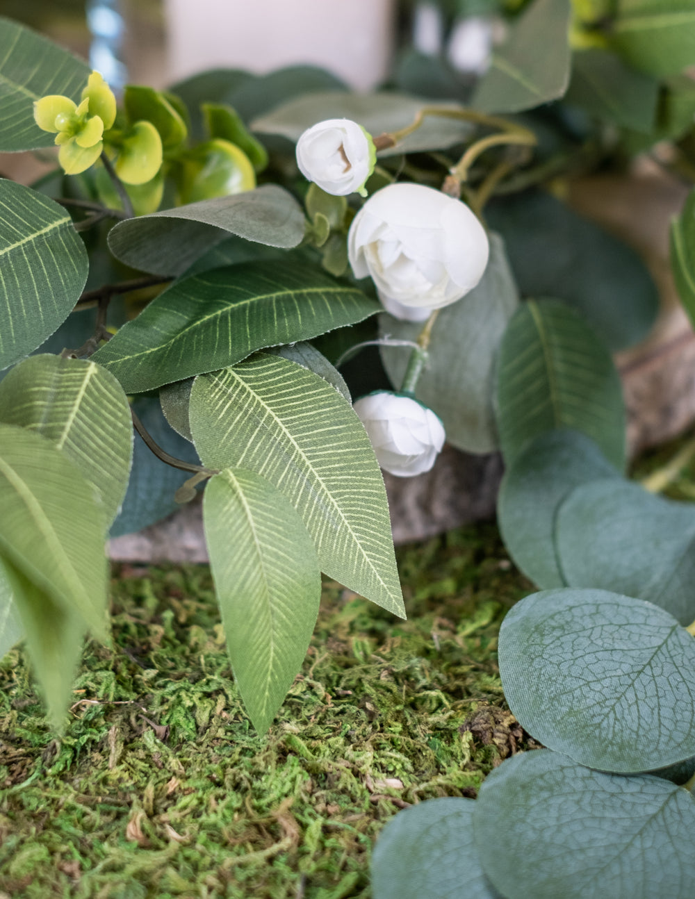 Gros plan sur les fleurs blanches et feuilles du chemin de table végétal en mousse naturelle pour mariage