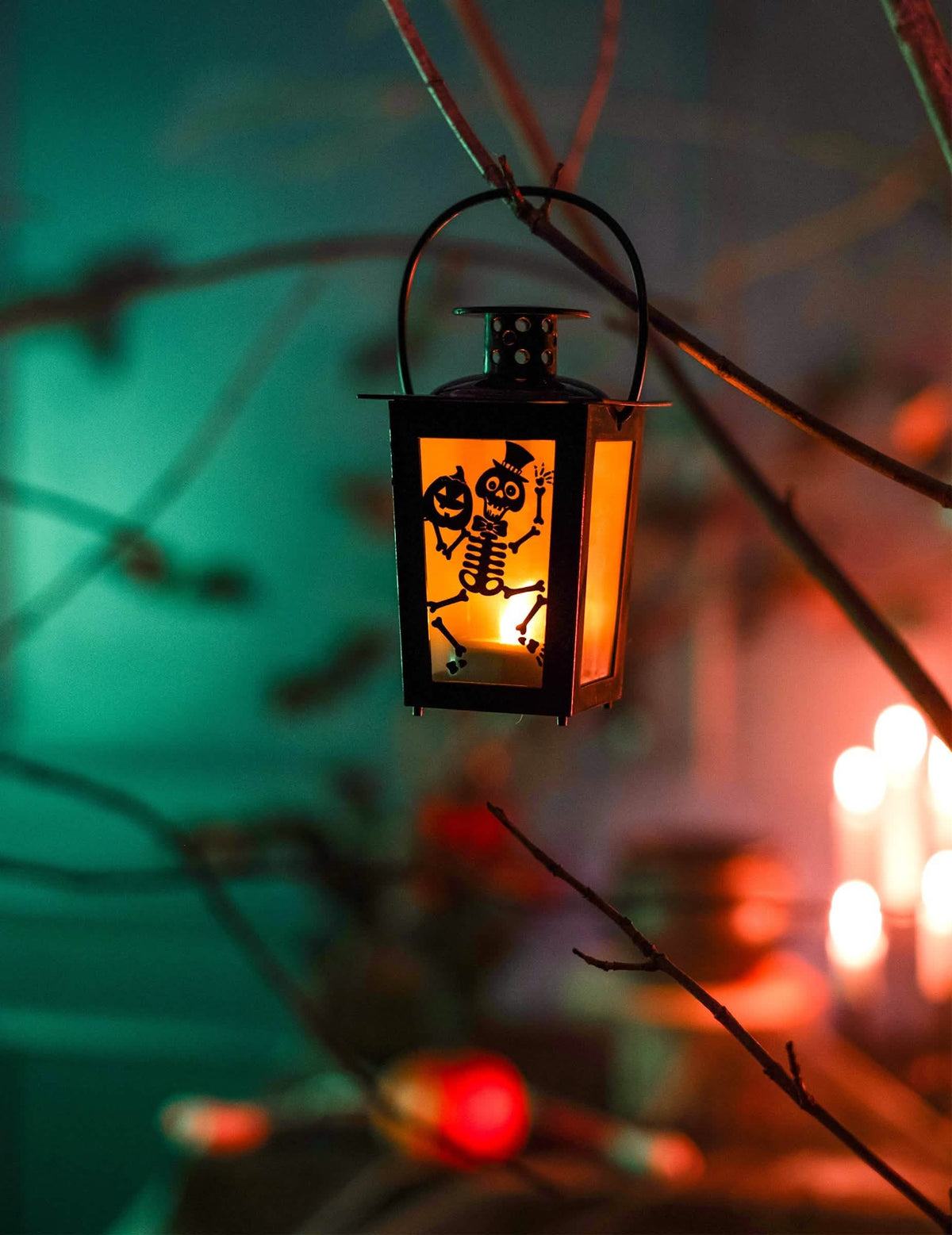 Závesná dekorácia na konári svietiaceho halloween lampáša so kostrou a tekvicou
