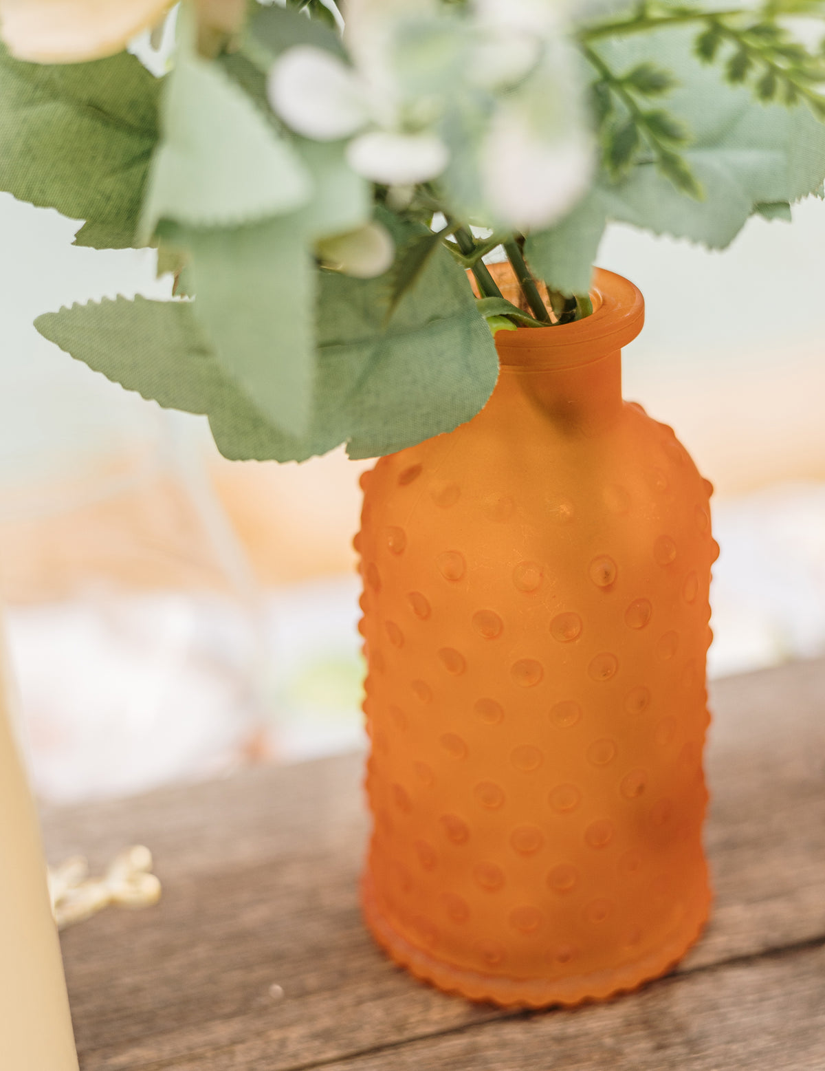 Gros plan sur le goulot et les fleurs du vase en verre texturé à pois en relief orange